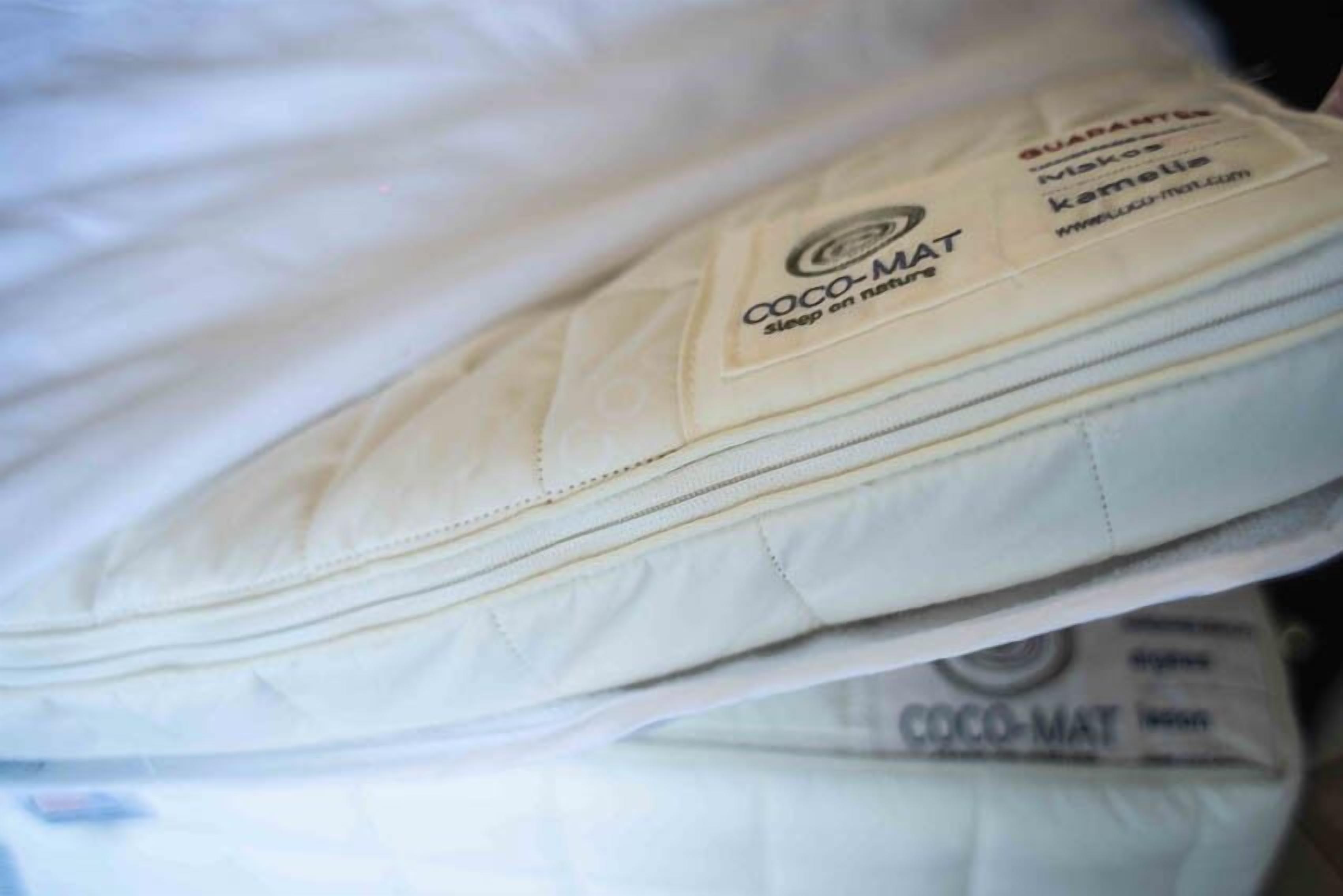 Ein Stapel weißer Matratzen mit dem Aufdruck 'COCO-MAT Sleep in Nature'.