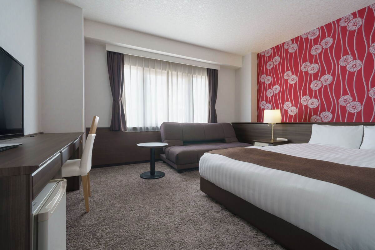Una habitación de hotel con cama, escritorio, silla, mesita, sofá y televisión.