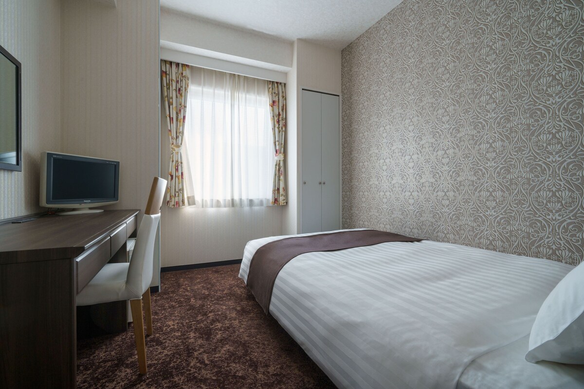 Habitación de hotel con una cama, un escritorio con computadora, una silla y un armario.