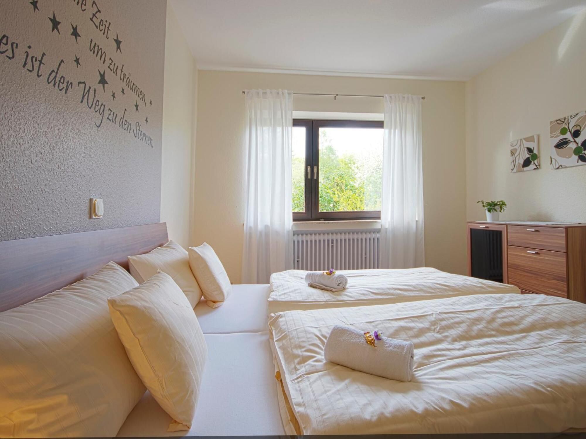 Ein Hotelzimmer mit zwei Betten, einem fensterbelaubten Fenster, einem Heizkörper und einer Wand mit Sternenaufschrift.