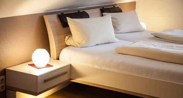 Un lit bien fait, avec du linge de lit blanc, une lampe de chevet et une tête de lit en bois.