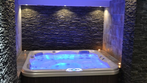 A hot tub with a stone wall backdrop, illuminated by blue lighting. - Wellness Hotel Sauna (Mala Moravka)