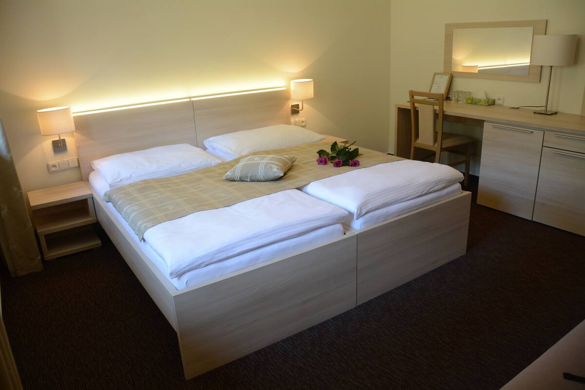 A double bed with a wooden headboard, bedside tables, a desk with a chair, a mirror, and a lamp.