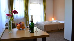 A hotel room with a bed, a bedside table with a bottle of champagne, a bowl of fruit, and a vase with flowers. - Wellness Hotel Sauna (Mala Moravka)