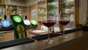 A bar area with two glasses of red wine, a beer tap, and a variety of bottles and glasses in the background. - Wellness Hotel Sauna (Mala Moravka)