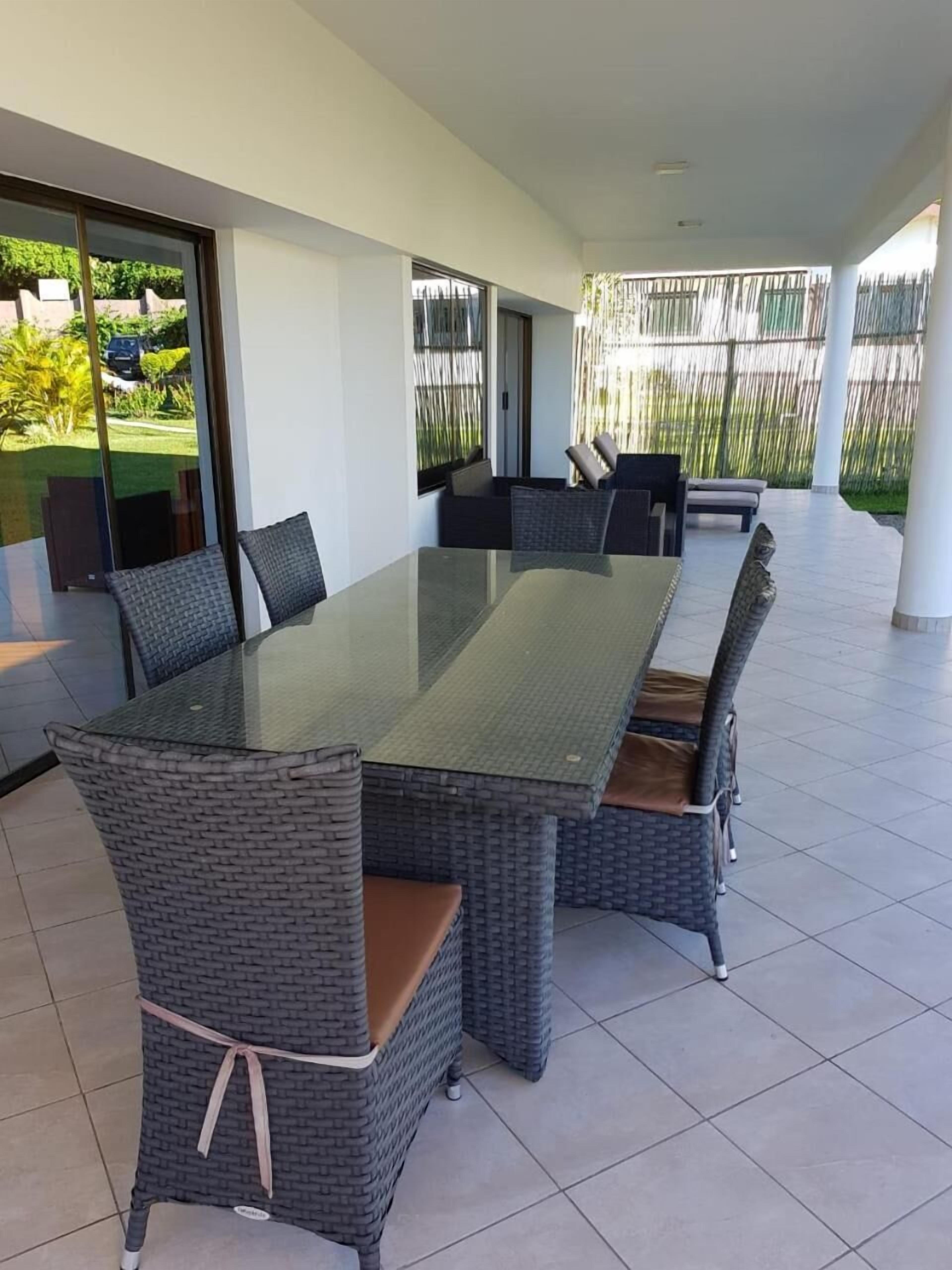 Un área de comedor al aire libre, moderna, con una mesa de vidrio y sillas de mimbre.