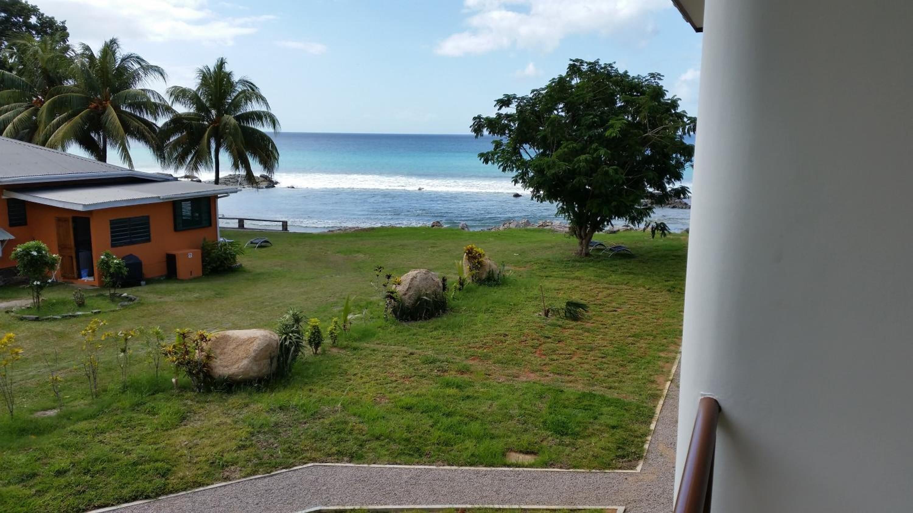 A view of a grassy area with a building, palm trees, and a beach.