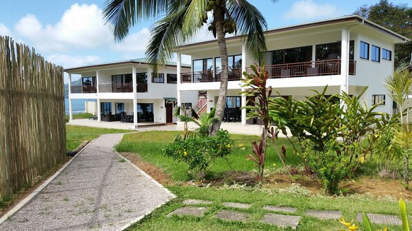 A two-story building with balconies, a paved walkway, and a grassy area with plants. - Beach Cottages  (Mahé Island)