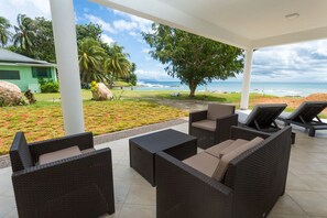 A covered outdoor seating area with wicker furniture and a view of the beach. - Beach Cottages  (Mahé Island)