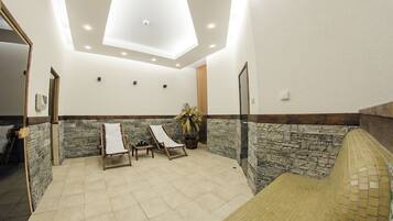 A spa room with two wooden loungers, a stone wall, a ceiling skylight, and a tiled floor.