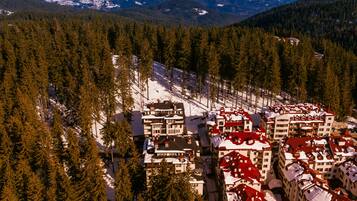 A snow-covered mountain resort with multiple buildings, dense forest, and a clear view of the surrounding mountains.