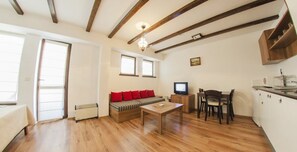 A cozy living room with a wooden floor, a sofa with red cushions, a television, and a dining area with chairs and a table. - Green Life Family Apartments Pamporovo (Chepelare)