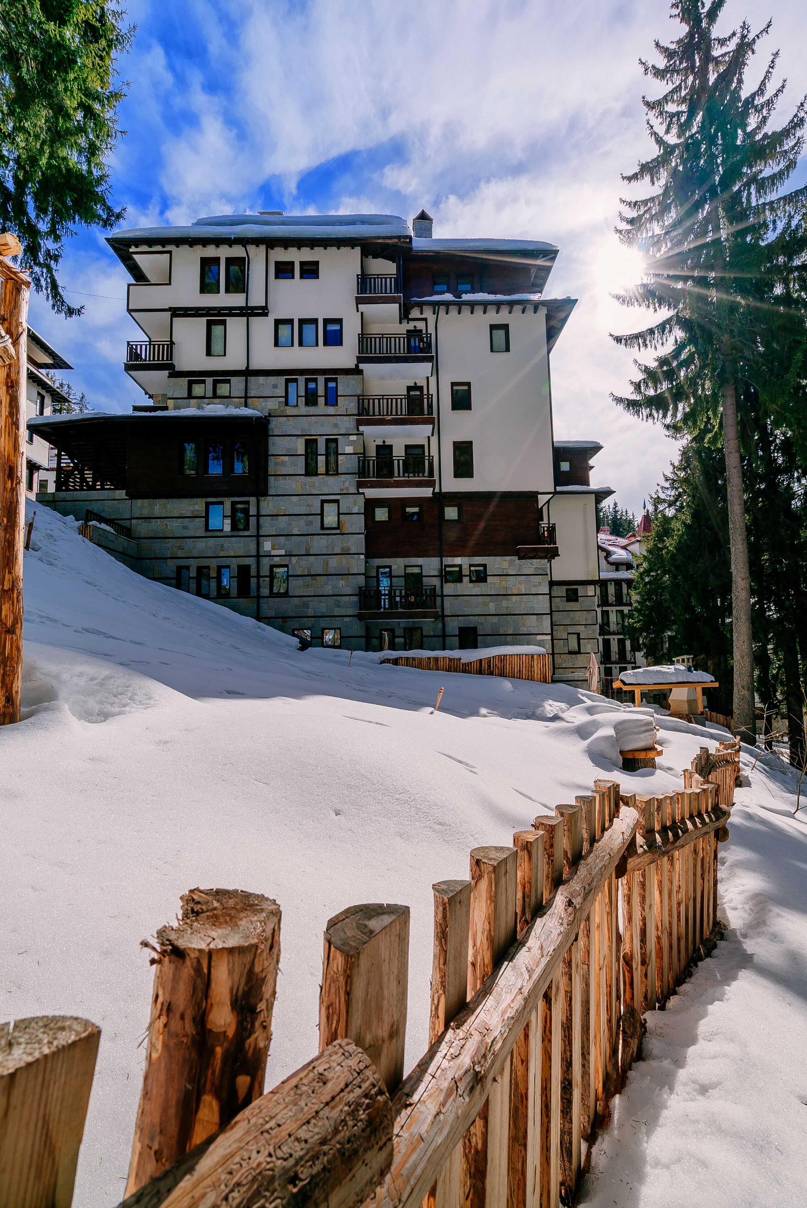 Un hotel de varios pisos con balcones, ubicado en una ladera nevada con pinos.