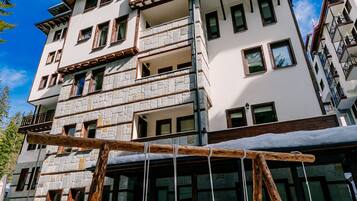 Een meerlaags gebouw met balkons, een houten schommelset op de voorgrond en sneeuw op de grond.