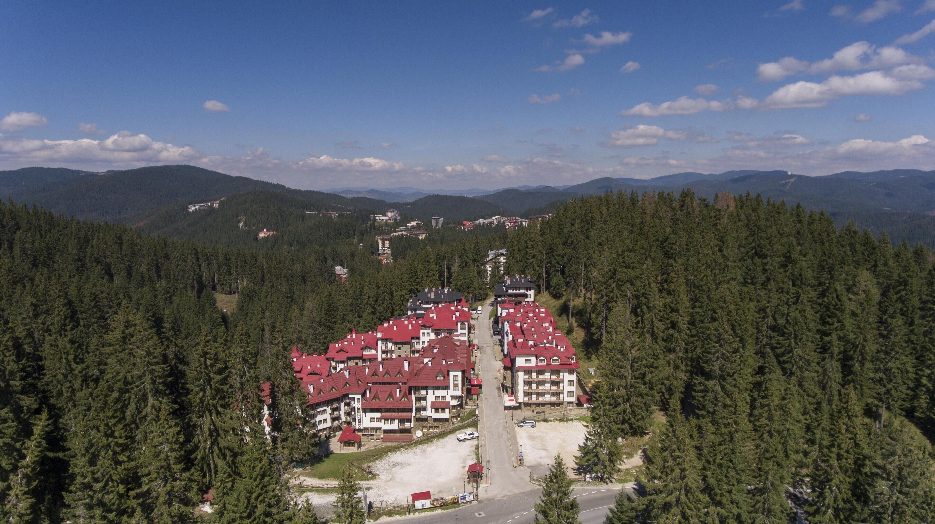 A residential area with red-roofed buildings surrounded by dense forests.