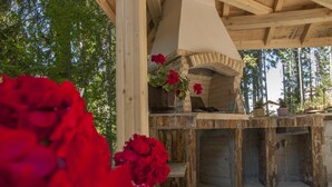 Un área de cocina exterior con horno de piedra, vigas de madera y flores rojas en macetas.