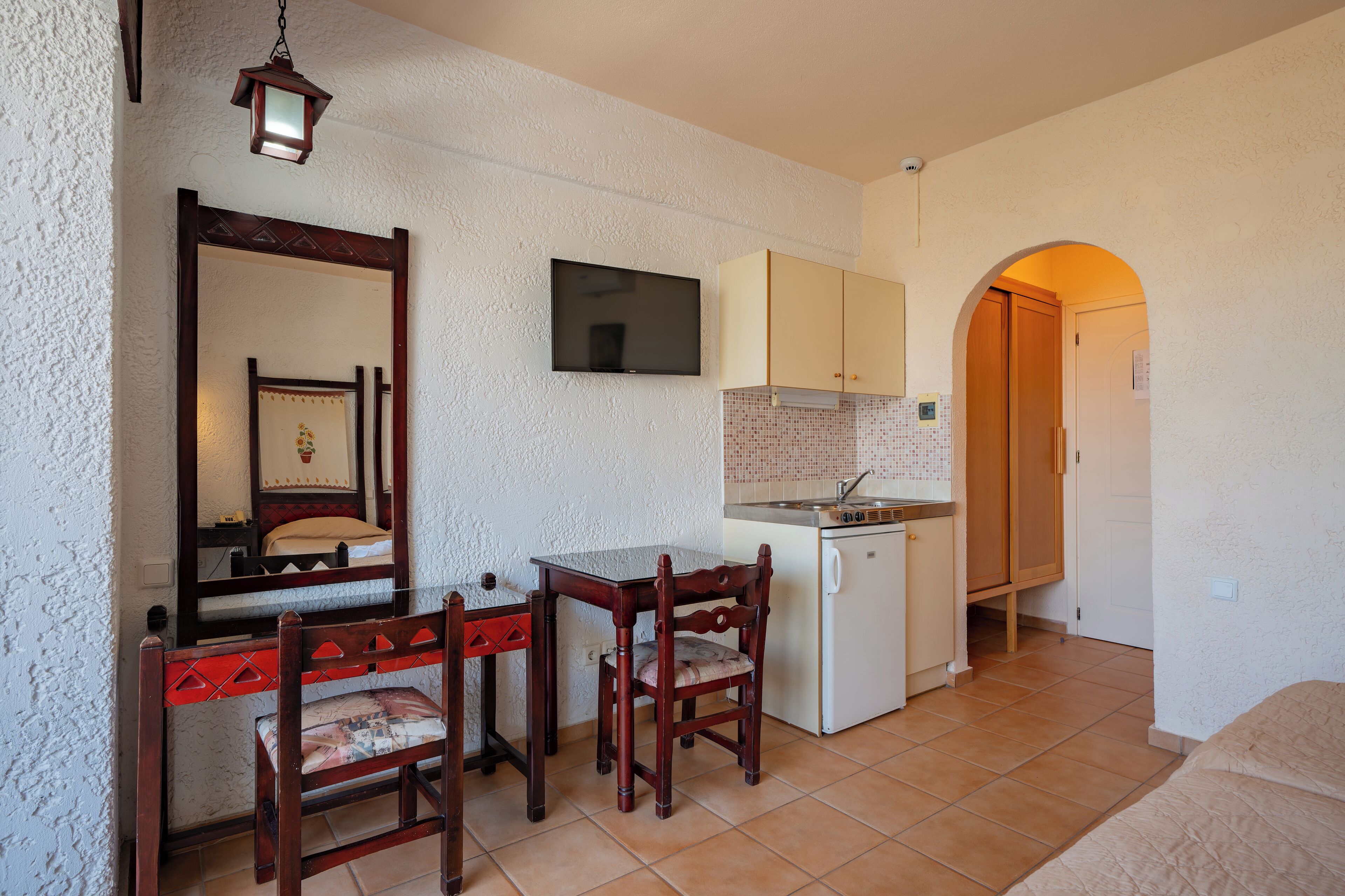 Un espacio habitable compacto con kitchenette, comedor con mesa y sillas, un espejo y un televisor.