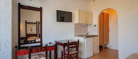 Un espacio habitable compacto con kitchenette, comedor con mesa y sillas, un espejo y un televisor.
