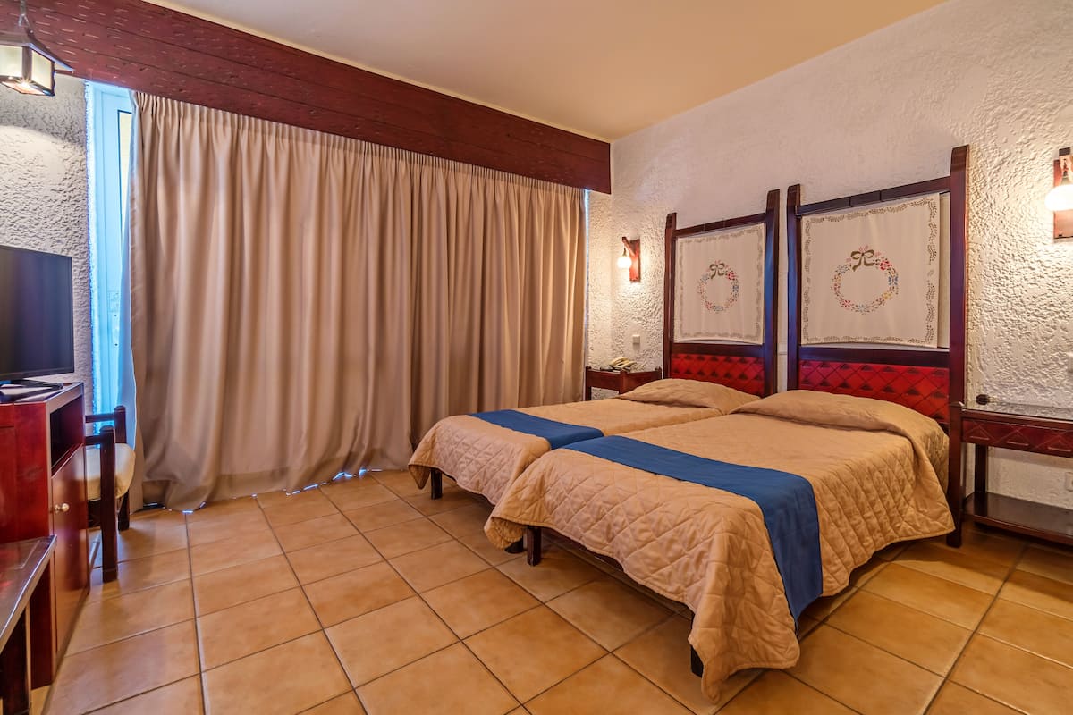 A hotel room with two beds, a TV, a desk, and a window with curtains.
