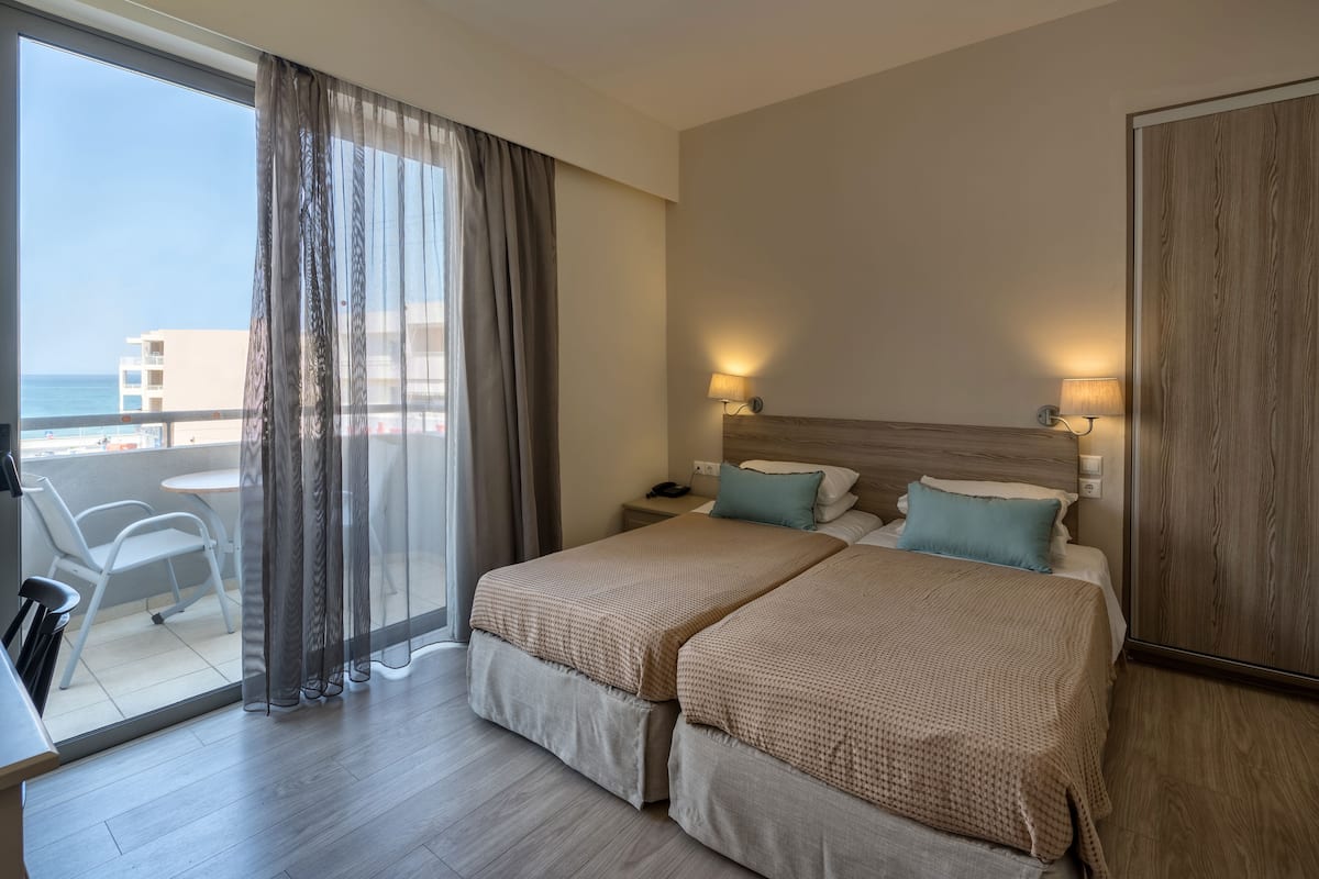 A hotel room with two beds, a balcony with a table and chairs, and a view of the sea.