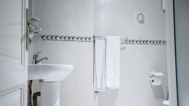 A bathroom with a white sink, a towel rack with a white towel, a toilet, and a shower area.