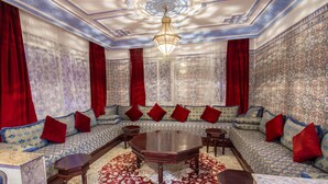 A luxurious room with a patterned wall, a large sofa with red cushions, a wooden coffee table, and a chandelier. - Hotel Tarek (Chefchaouen)