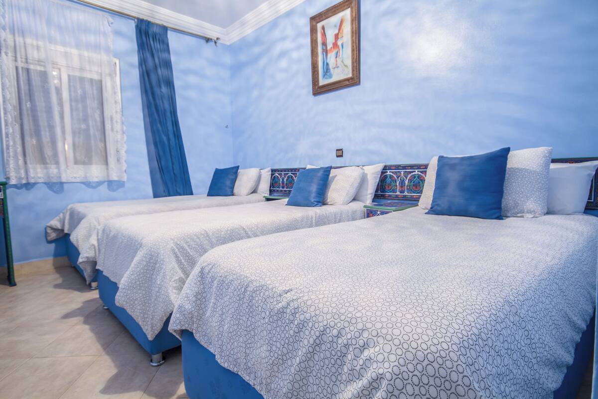 A room with two beds, each with a patterned bedspread and blue pillows.
