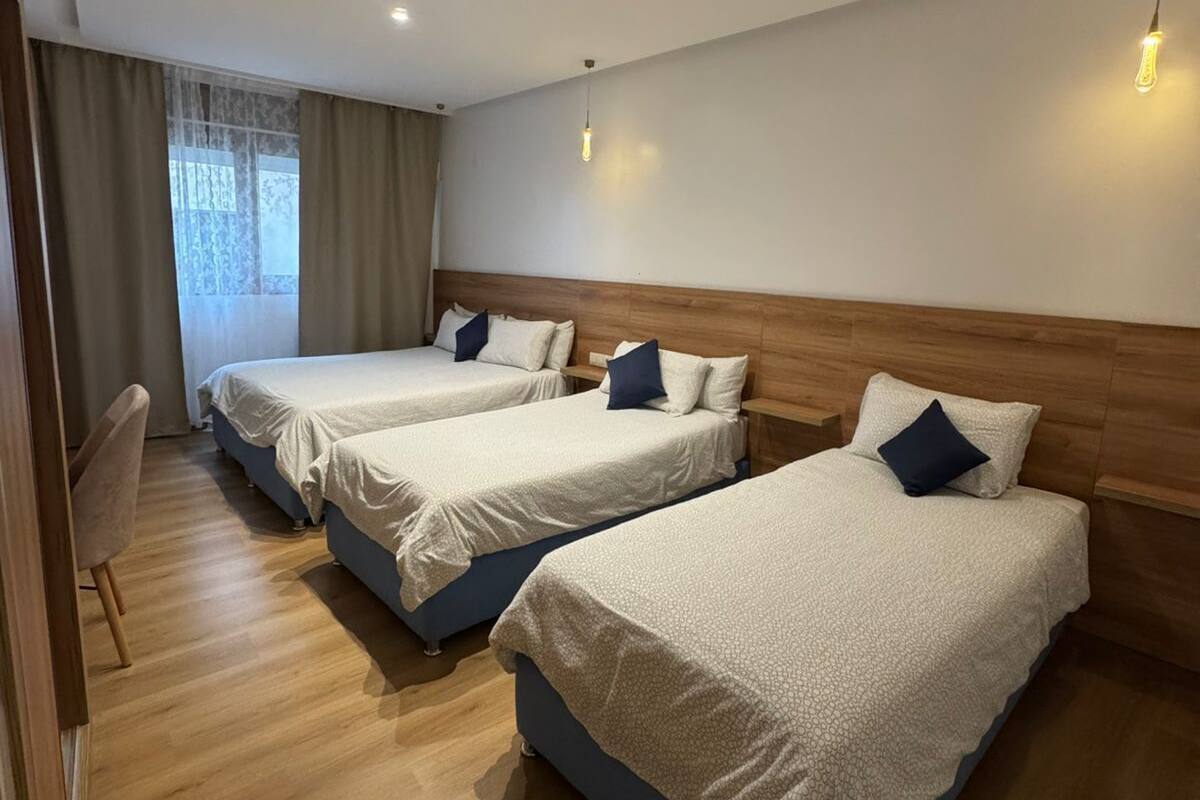 A hotel room with three beds, wooden headboards, and a view of the outdoors.