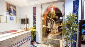 A reception area with a marble counter, potted plants, and a glass door leading to a corridor. - Hotel Tarek (Chefchaouen)
