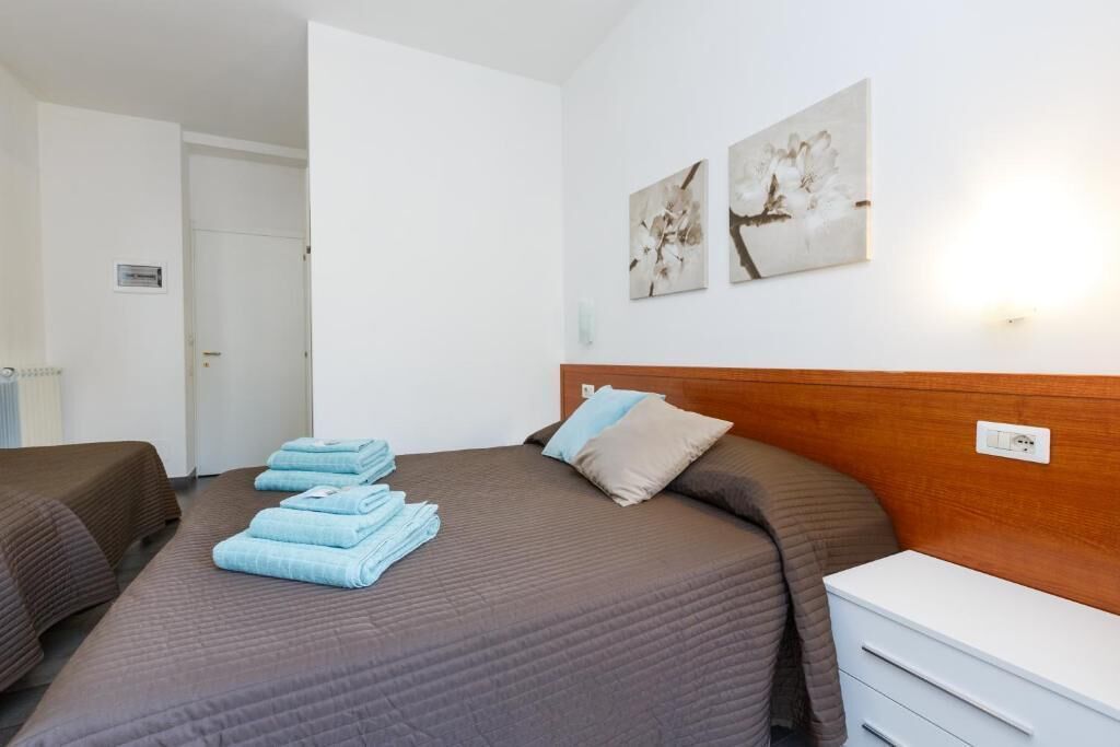 A hotel room with a bed, two bedside tables, a wardrobe, and artwork on the wall.