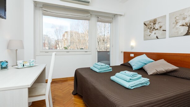 Habitació d'hotel amb un llit, una taula de treball i una finestra amb cortines.