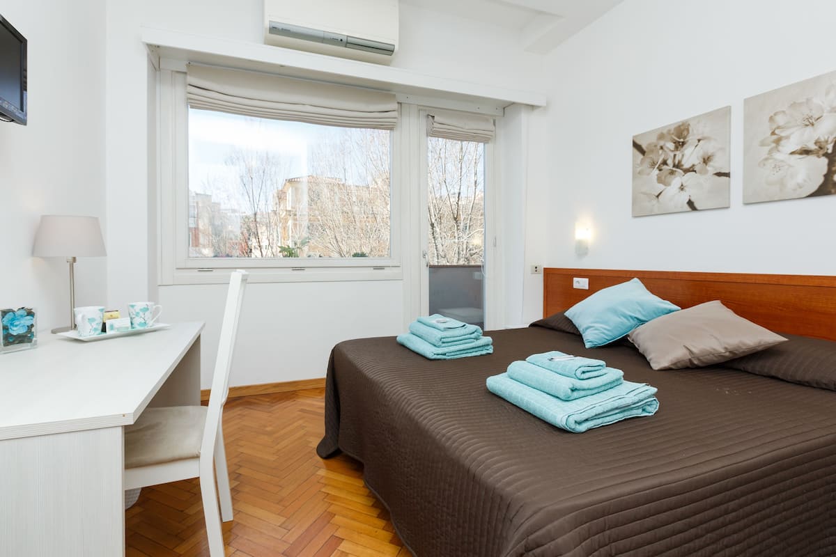 A hotel room with a bed, a desk, and a window with curtains.