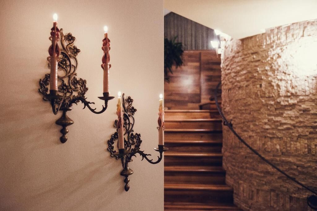 A wall-mounted candelabra with three lit candles, a staircase with wooden steps, and a textured stone wall.