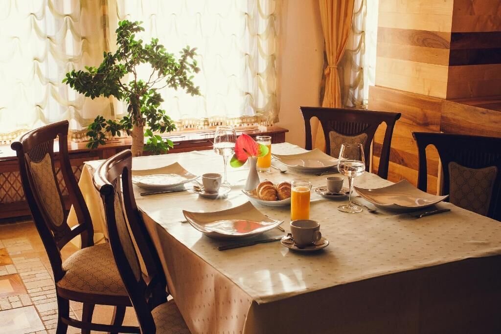 A breakfast table set with plates, cups, and a glass of orange juice, surrounded by wooden chairs.