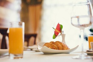 Une table mise pour le petit-déjeuner avec un croissant sur une assiette, un verre de jus d’orange et un verre d’eau.