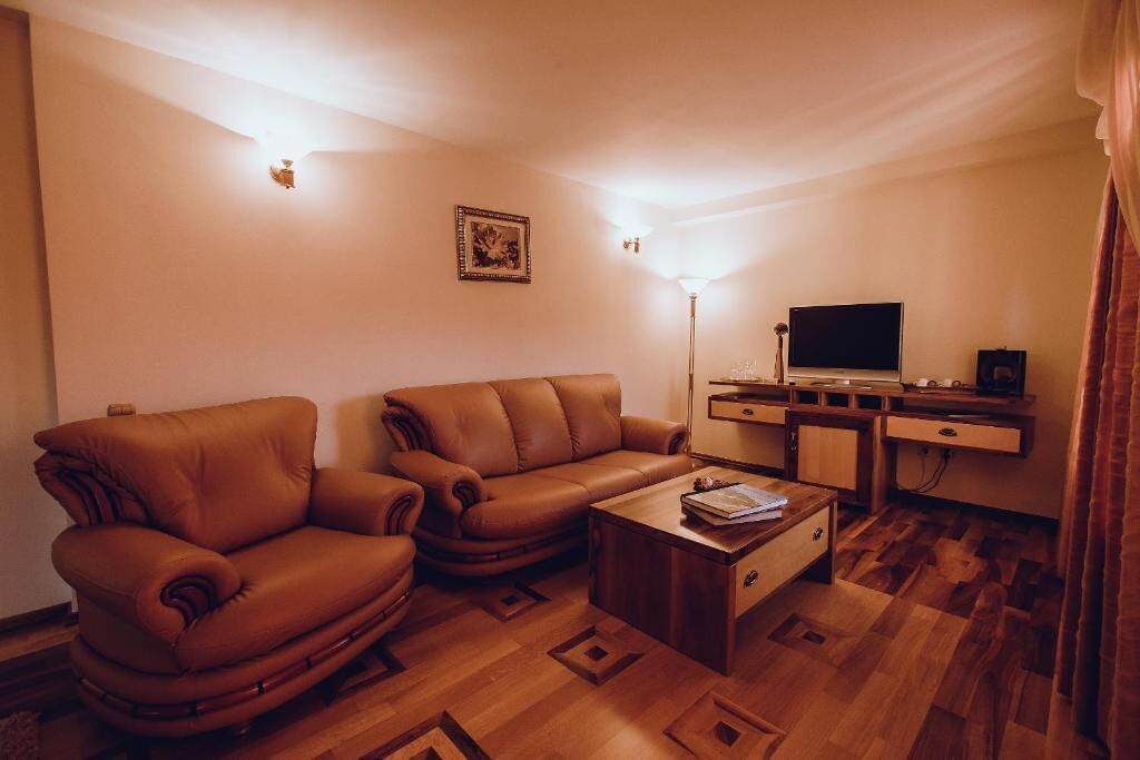 Een woonkamer met een bruine leren bank, een houten salontafel en een flatscreen televisie op een houten dressoir.