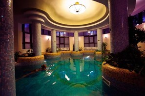 An indoor swimming pool with clear water, surrounded by columns and plants, and a ceiling light fixture. - Denisa Boutique (Brasov)
