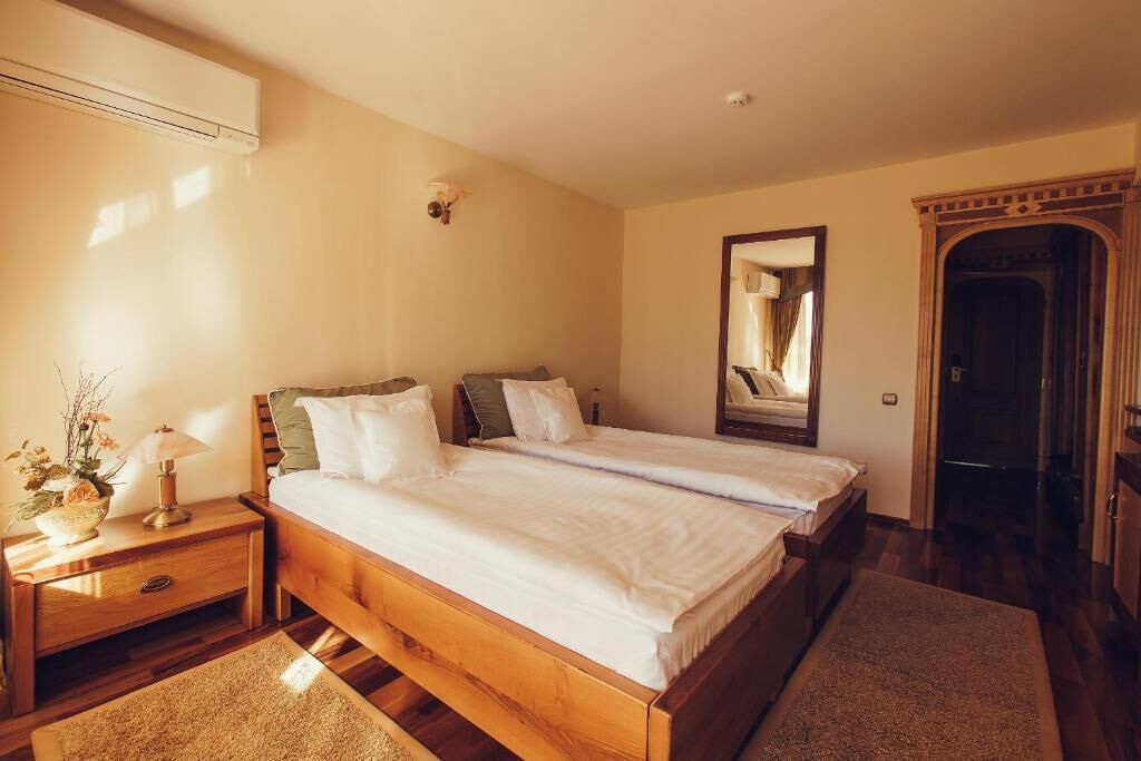 A bedroom with two single beds, a nightstand with a lamp, a mirror, and a wooden wardrobe.