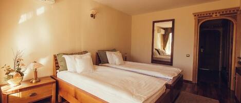 A bedroom with two single beds, a nightstand with a lamp, a mirror, and a wooden wardrobe.