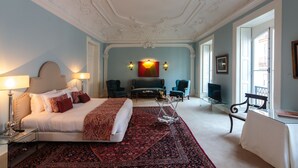 Une chambre spacieuse avec un grand lit, un coin salon comprenant un canapé et des fauteuils, une télévision et un tapis décoratif.