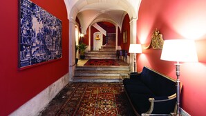 Un couloir aux murs rouges, une décoration murale faite de carreaux bleus et blancs, un escalier, une moquette à motifs, un canapé bleu foncé et une lampe.