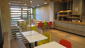 Una cafetería con varias mesas y sillas, un mostrador con productos alimenticios, y una pared decorativa.
