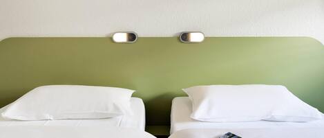 A hotel room with two beds, each with white bedding and pillows. There is a green accent wall above the beds, and a small painting of grass.