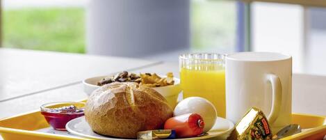A breakfast tray with a croissant, a boiled egg, a red sausage, a glass of orange juice, a mug, and a small container of butter.