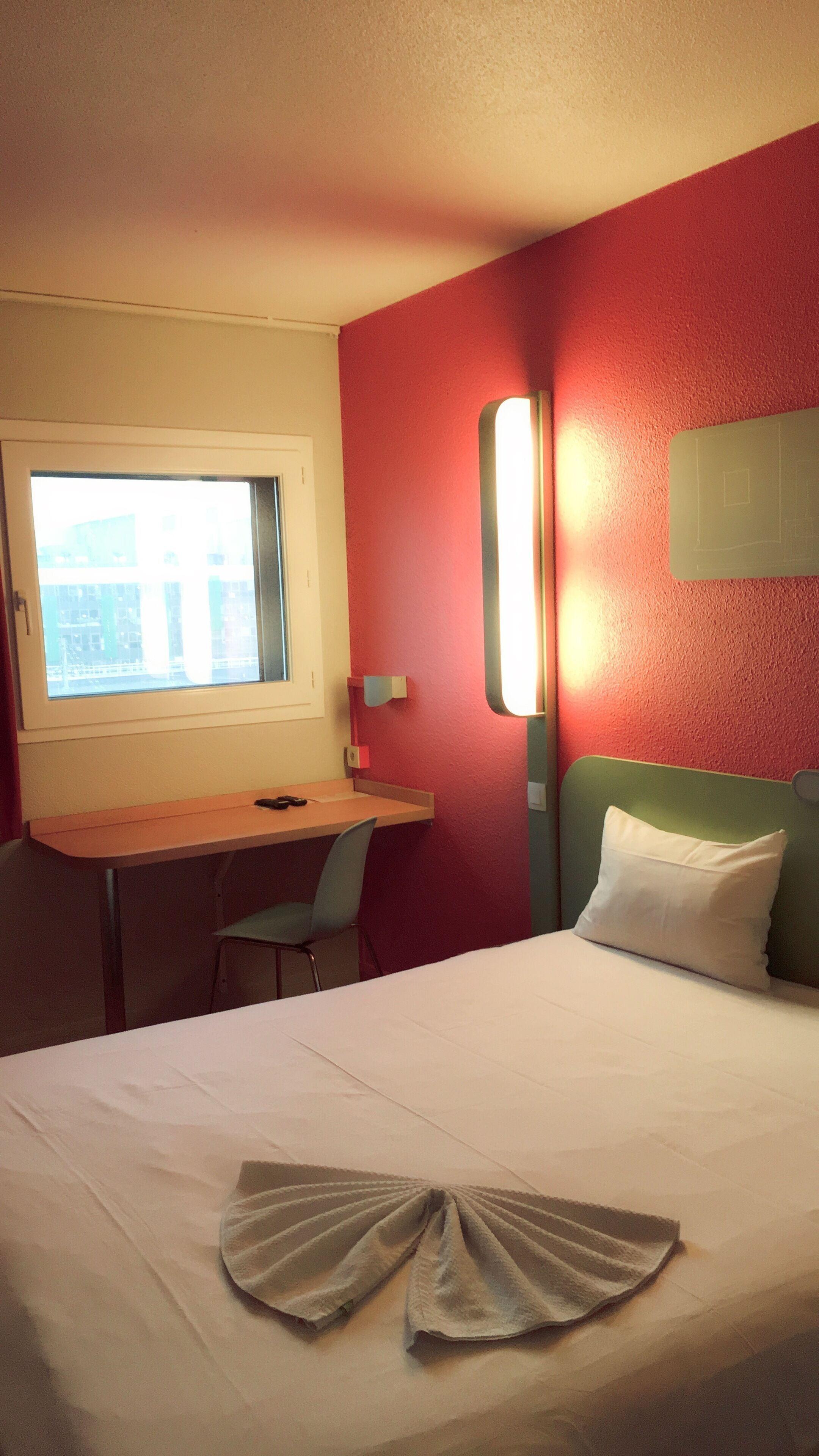 A hotel room with a bed, a desk, a chair, and a window.