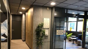 Un interior moderno con una recepción, una planta en maceta y un área de estar con mesas y sillas.