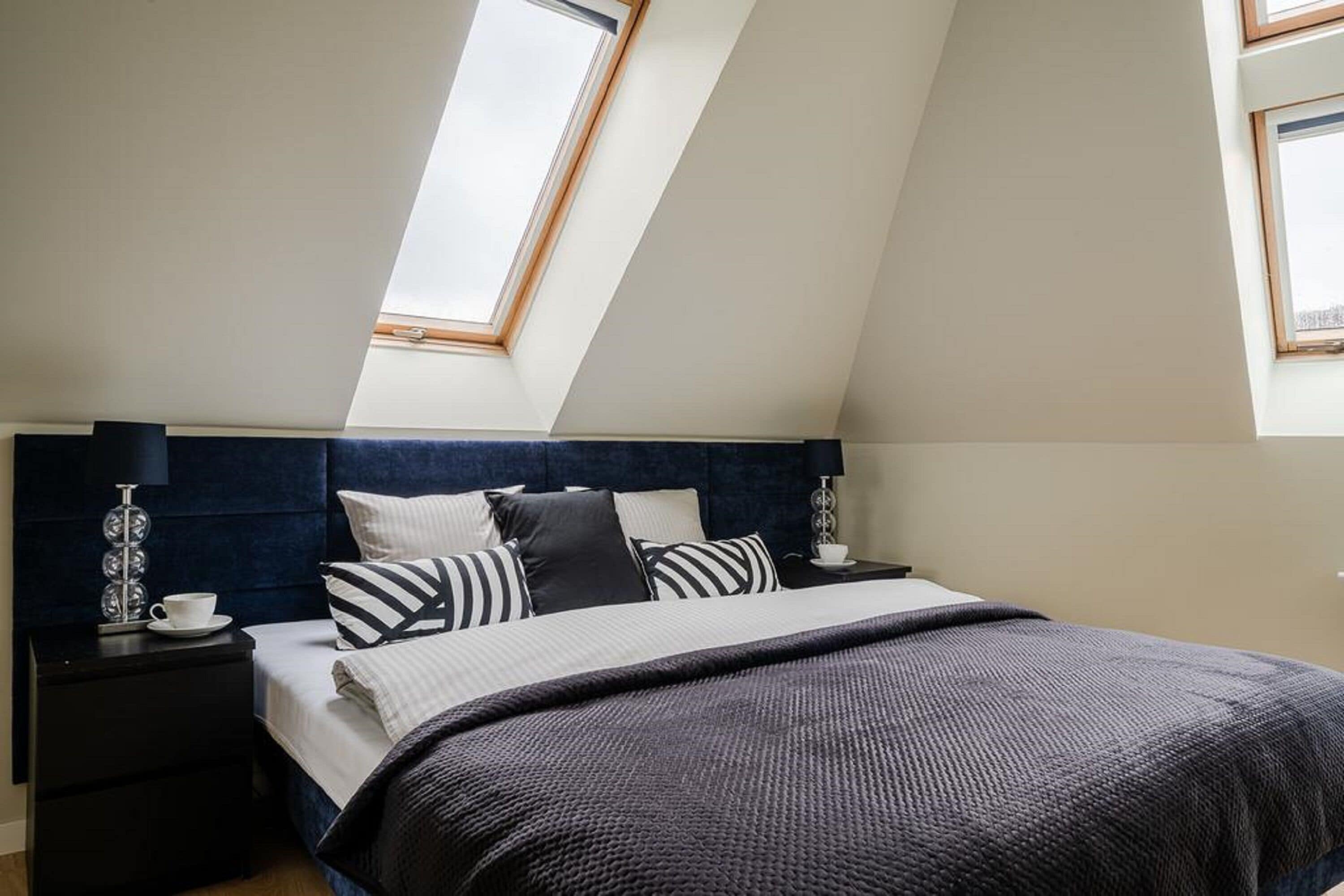 A bedroom with a sloped ceiling, a bed with a dark headboard, and two bedside tables with lamps.