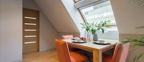 Un comedor con una mesa de madera, sillas naranjas, un florero con flores y vistas a través de un tragaluz.