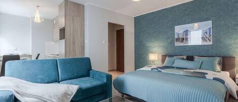 Una habitación de hotel moderna con un sofá azul, una cama grande con almohadas a juego y un cuadro en la pared.