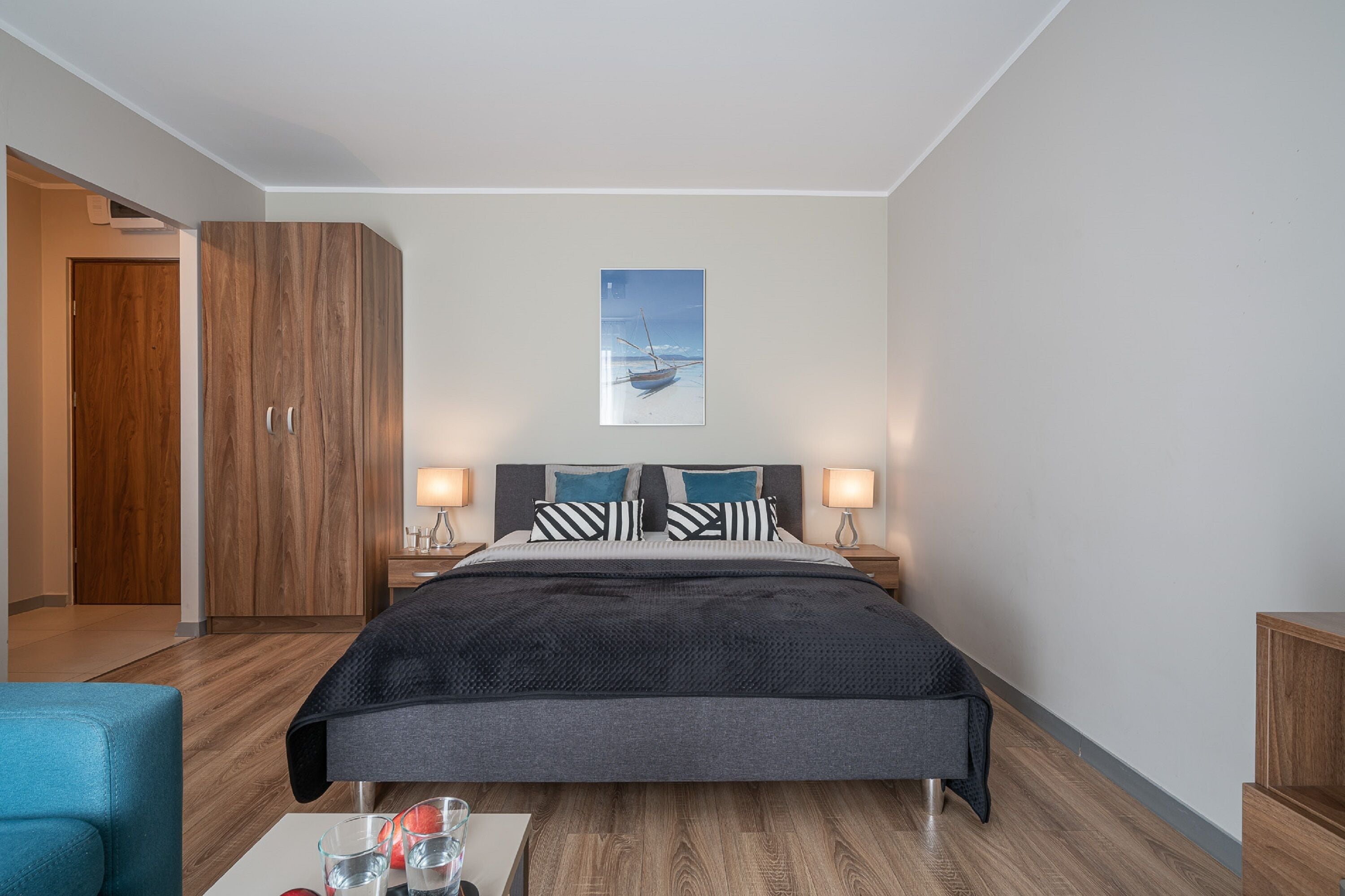 A modern hotel room with a large bed, wooden wardrobe, bedside lamps, and a framed picture on the wall.